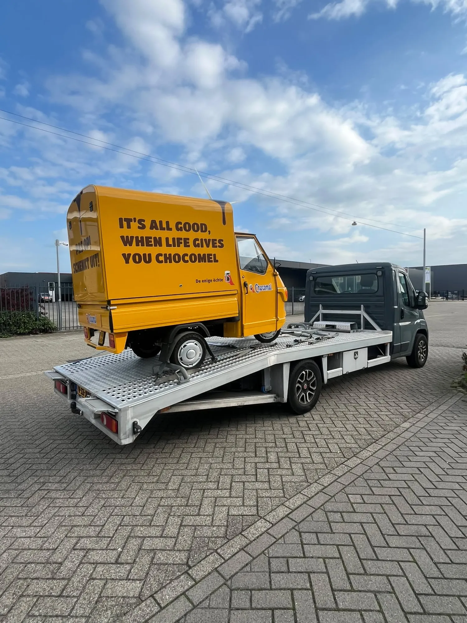Gele Piaggio Ape promotiewagen van Chocomel vastgezet op de oprijwagen van Snel Autotransport