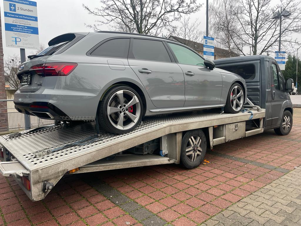 Grijze Audi stationwagon op een autoambulance bij Duitse parkeerborden, klaar voor transport naar Nederland